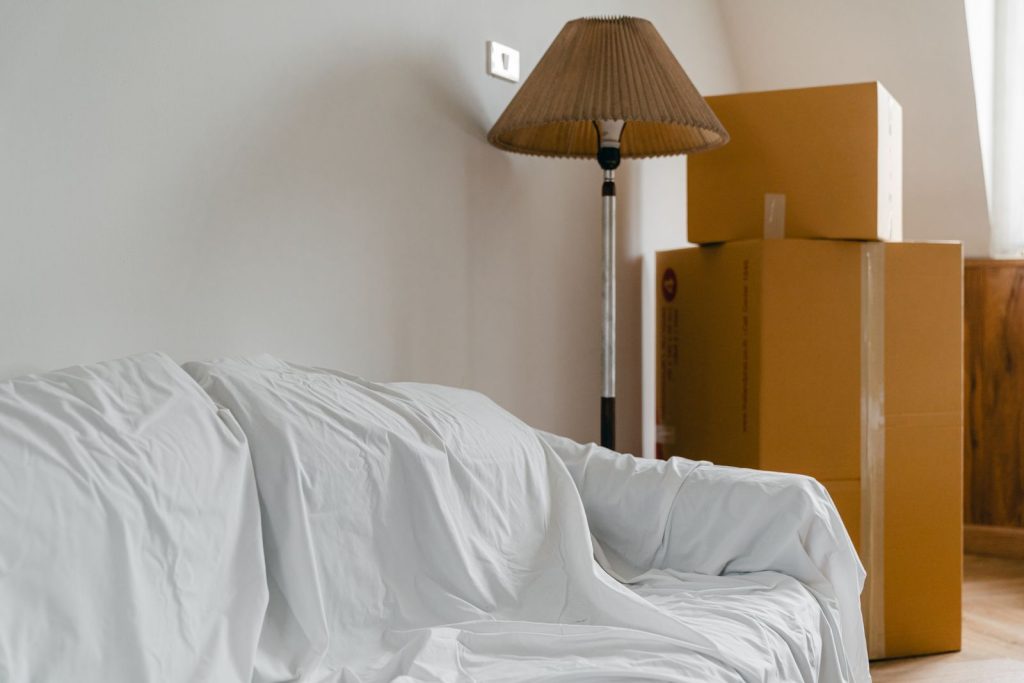 canapé protégé par un drap et cartons empilés dans une pièce vidée avant des travaux