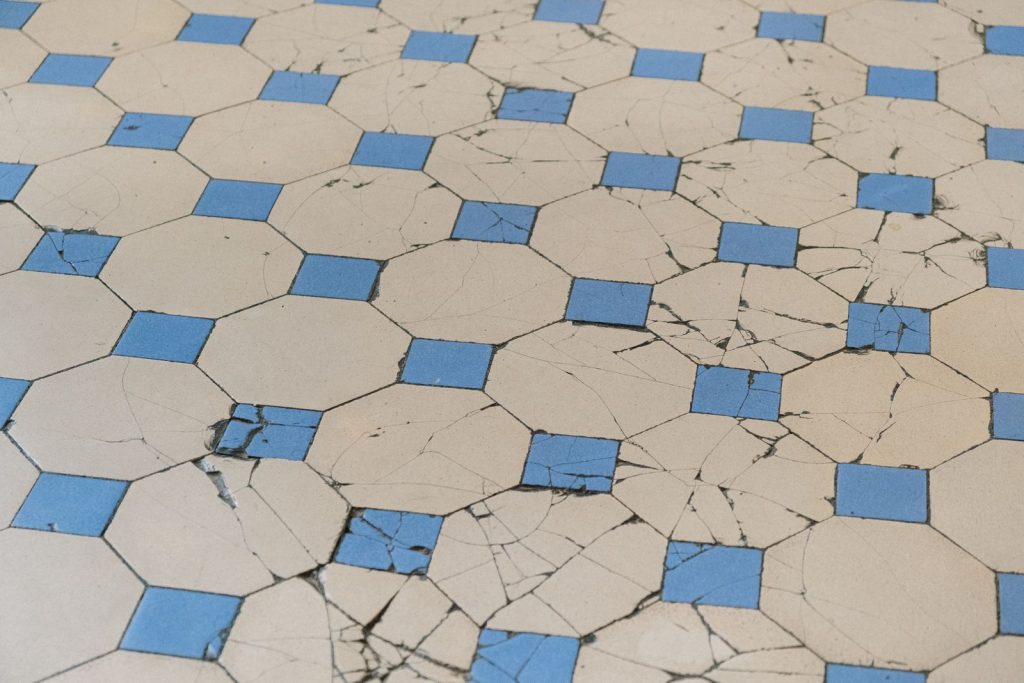 Carrelage ancien fissuré au motif géométrique bleu et blanc.