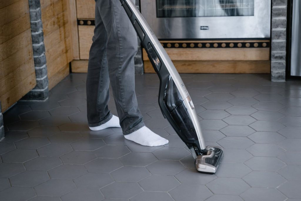 Personne passant l’aspirateur balai sur un sol carrelé sombre