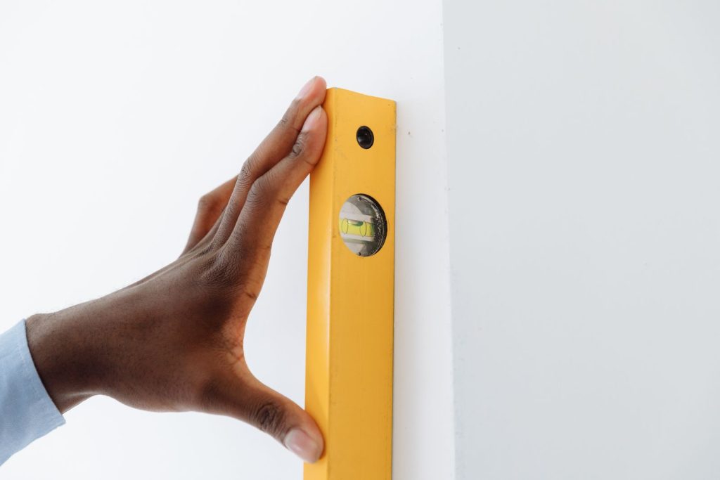 Main utilisant un niveau à bulle jaune contre un mur