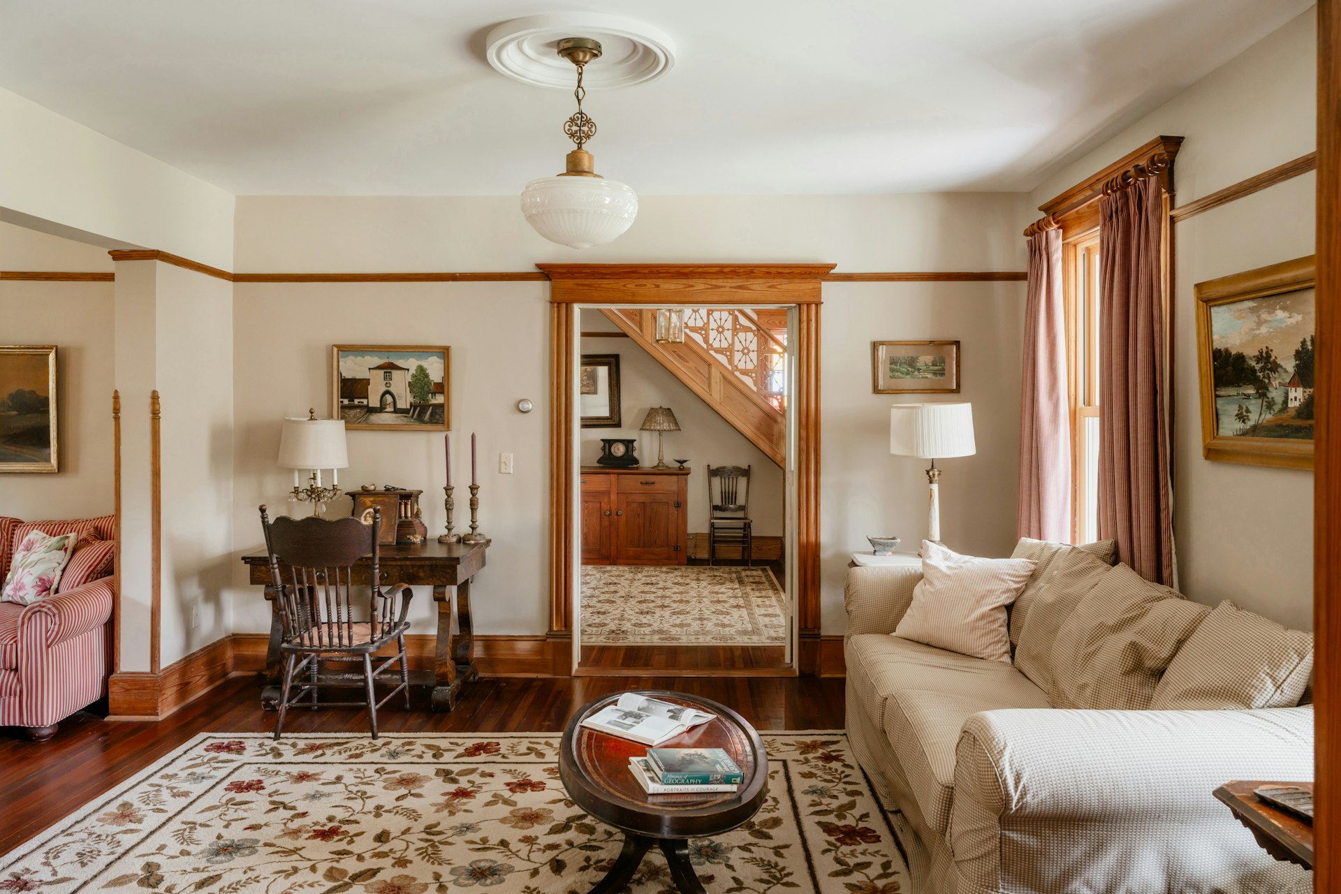 salon avec suspension en verre au plafond, lampes à poser à abat-jour blanc et grand tapis à fleurs sur parquet foncé