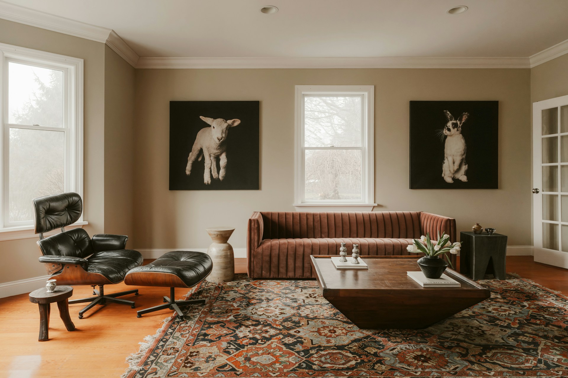salon avec un grand tapis persan rouge, un canapé brique et deux tableaux d'animaux sur fond noir